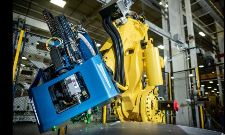 A large yellow industrial robot fitted with a blue end-effector in a plant